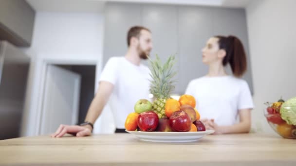 Mladý veselý pár v kuchyni diskutovat o ovoce a zelenině — Stock video
