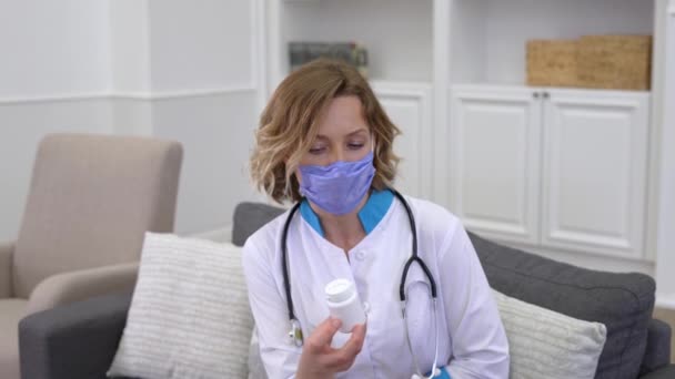 Jovem médico vestindo máscara protetora prescrevendo medicamentos para o paciente durante a visita domiciliar — Vídeo de Stock