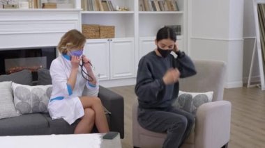 Koruyucu maske takan genç kadın hasta akciğerlerini steteskopla kontrol ediyor.