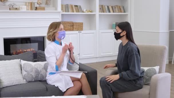 Kvinnlig läkare bär ansiktsskydd mask kontrollera patientlungor med stetoskop när du besöker klienten hemma — Stockvideo