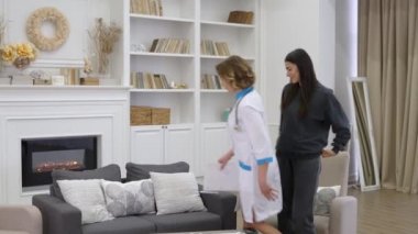 Kadın doktor, oturma odasında birlikte otururken hasta kadının şikayetlerini dikkatle dinliyor.