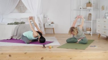 Young woman and yoga instructor stretching during private class