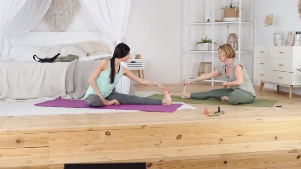 Дружелюбный тренер по йоге учит молодых женщин растягивать свое тело — стоковое видео