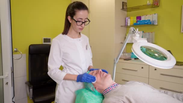 Cosmetólogo limpiando la piel del cliente senior antes del procedimiento de belleza anti edad — Vídeo de stock