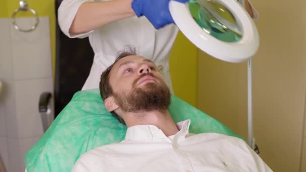 Kosmetikerin bereitet Klient auf Haarmesotherapie in Klinik vor, diskutiert mit Mann kosmetische Behandlung von Haarausfall — Stockvideo