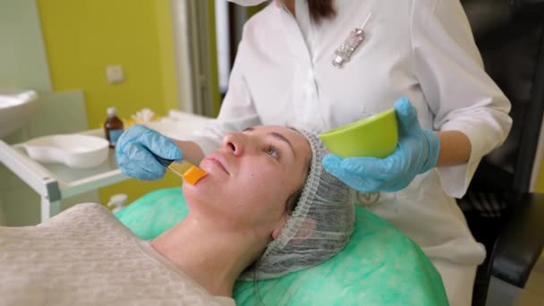 Vrouwelijke cosmetoloog voert fruit zuur peeling procedure voor jonge vrouwen in schoonheidskliniek — Stockvideo