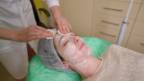 Female beautician cleaning face of young woman from cosmetic mask — Stock Video