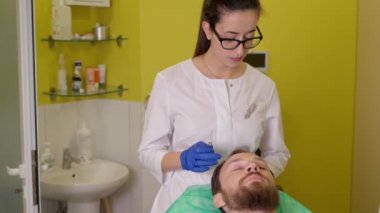 Kozmetik uzmanı adamı güzellik kliniğinde saç terapisi prosedürüne hazırlıyor.