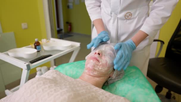 Cosmetologist applying wet disposable towels on woman face with cosmetic cream or mask — Stock video