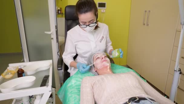 Kosmetička nanáší obličejovou masku na kůži mladé ženy klienta během peelingu ovocné kyseliny — Stock video