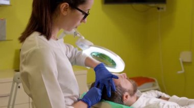 Güzellik uzmanı, kozmetoloji kliniğinde saç terapisi için hastayı hazırlıyor.