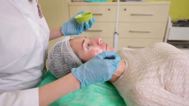 Esteticista aplicando ácido de frutas con cepillo de cuenco en la piel de la cara de la mujer joven — Vídeos de Stock