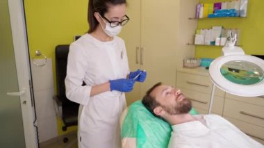 Klinikteki genç adam için saç terapisi prosedürü yapan bir doktor.