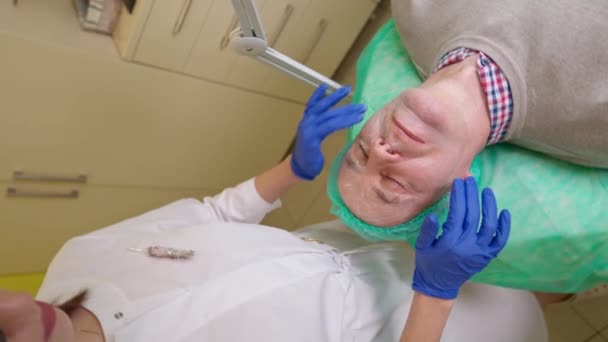 Cosmetologist fêmea que aplica a pele anestésica da nata do homem maduro durante o procedimento injetável antiidade — Vídeo de Stock