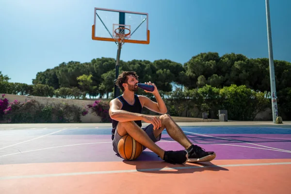 Tired Man basketball player drinks water after training. replenishment of water balance