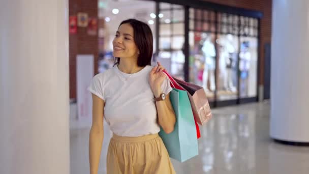 Joven mujer feliz caminando con confianza en el centro comercial con bolsas de papel en la mano — Vídeo de stock