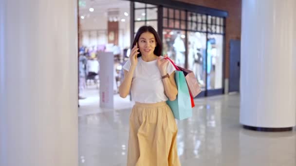 Vrouw praten over de telefoon met vriend terwijl het doen van winkelen in winkelcentrum — Stockvideo