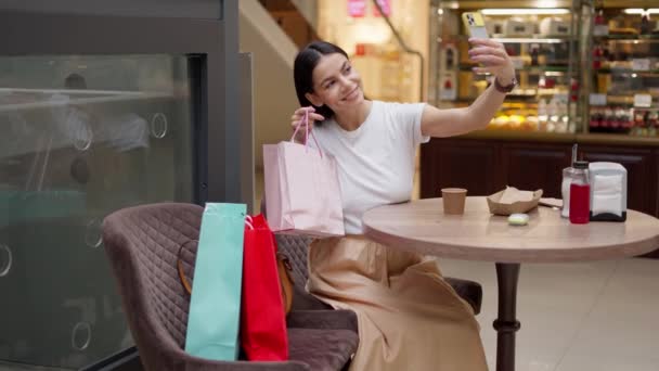 Очаровательный блогер моды делает селфи с бумажным пакетом в торговом центре — стоковое видео