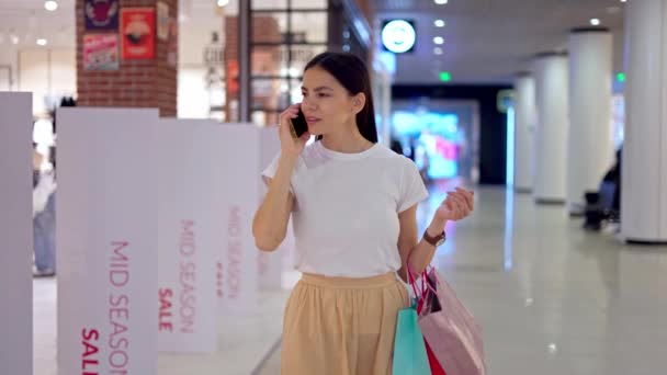 Kobieta rozmawia przez telefon komórkowy z przyjacielem podczas dnia zakupów w centrum handlowym — Wideo stockowe