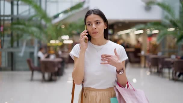 Жінка шопоголік розмовляє з другом на мобільному телефоні про одяг, який вона знайшла під час покупок — стокове відео