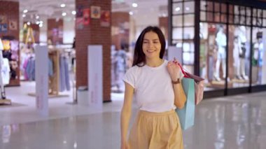 Alışveriş merkezinde kağıt torbalarla dolaşan mutlu bir kadın.