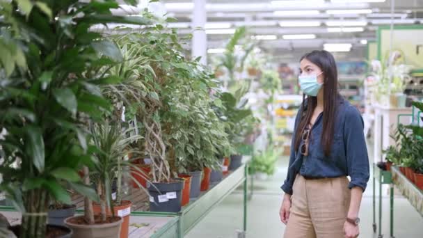 Młoda klientka nosząca maskę ochronną na twarz wybiera zieloną roślinę doniczkową — Wideo stockowe