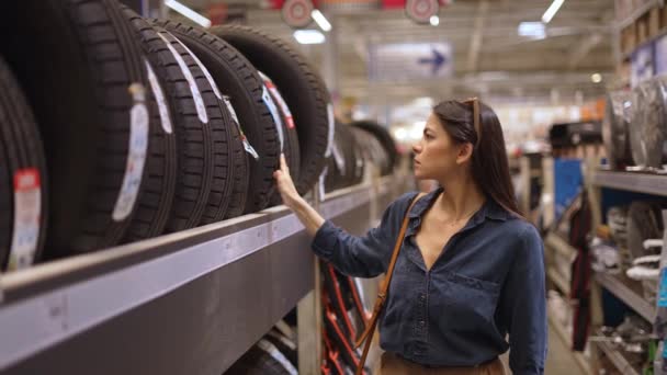 Mujer joven cliente compra neumáticos nuevos en el departamento con artículos de automóviles — Vídeo de stock