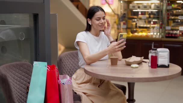 Mulher conversando via chat de vídeo no celular enquanto almoça depois de fazer compras — Vídeo de Stock