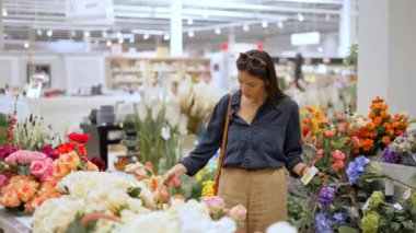Ev dekorasyonu bölümünde alışveriş yaparken yapay çiçeklerden buket yapan genç bir kadın.