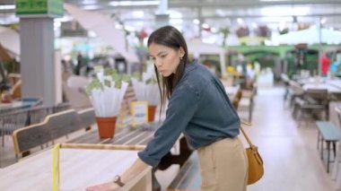 Bahçe için mobilya seçerken ahşap masa fiyatına bakan genç bir kadın.