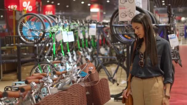 Joven cliente femenino eligiendo ciudad bicicleta con cesta para llevar cosas en tienda de deportes — Vídeo de stock