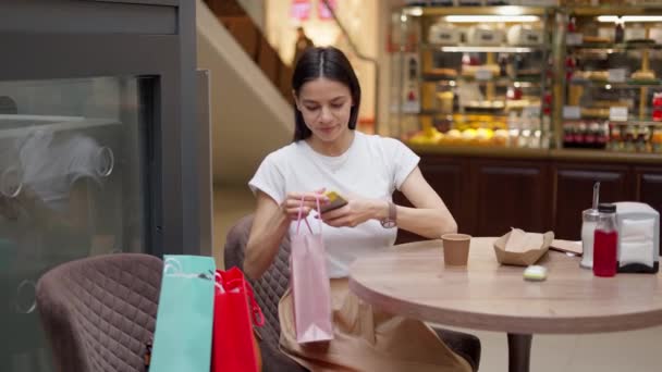 Vrouw het nemen van selfie met kleine boodschappentas terwijl zitten in cafe in winkelcentrum — Stockvideo