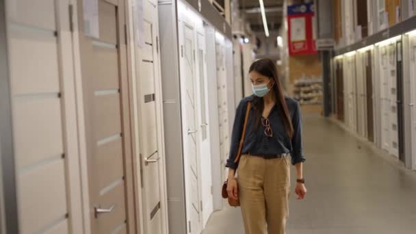 Молода жінка в захисній масці для обличчя купує нові дерев'яні міжкімнатні двері для дому — стокове відео