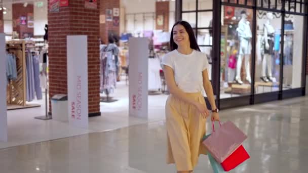 Gelukkige vrouw verlaat winkel in winkelcentrum met veel papieren tassen vol met aankopen — Stockvideo