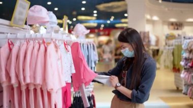 Yüzü maskeli genç bir kadın bebeğine kıyafet seçerken hassas duygular hissediyor.