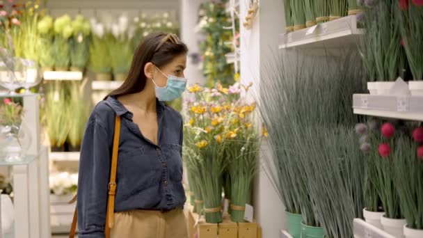 Giovane donna in maschera guardando verde decorativo pianta in vaso artificiale per l'arredamento della casa, l'acquisto di fiori falsi — Video Stock