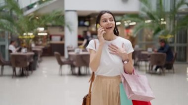 Alışveriş merkezinde alışveriş yaparken cep telefonuyla konuşan heyecanlı genç kadın.