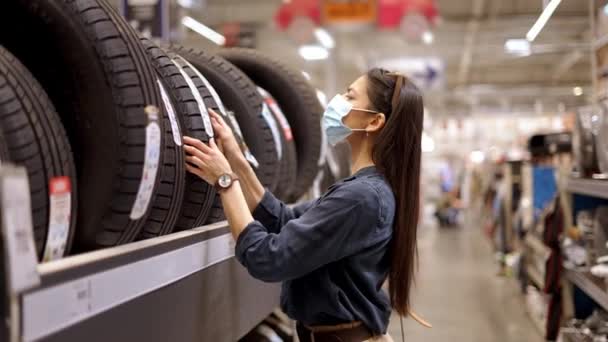 Mujer joven enfocada en la cara máscara médica examinar la marca y las características del producto al comprar neumáticos nuevos — Vídeo de stock