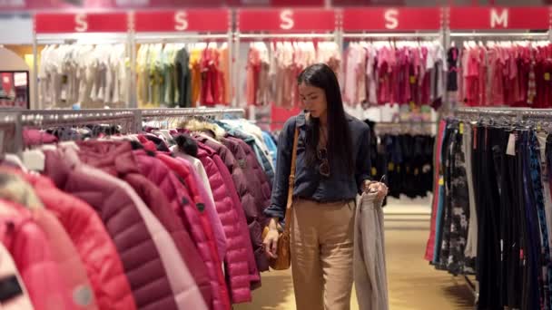 Jonge vrouwelijke klant op zoek naar vrouwen kleding op hangers, terwijl het doen van winkelen in de grote sport afdeling — Stockvideo