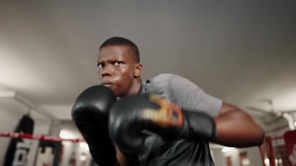 Jovem focado lutador masculino africano vestindo luvas de boxe preto dando socos no anel — Vídeo de Stock