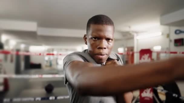 Jovem motivado desportista africano boxeador dando socos na câmera durante o treinamento de boxe no ginásio — Vídeo de Stock