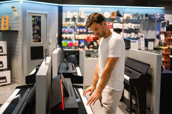 Внимательный клиент выбирает фортепиано в музыкальном магазине — стоковое фото