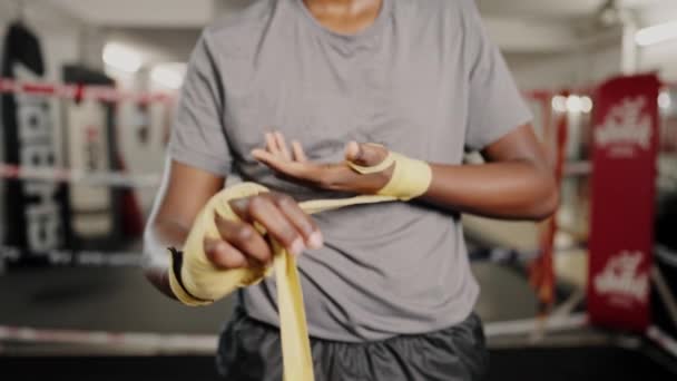Młody afrykański bokser w odzieży sportowej wiążący żółte bandaże bokserskie przed ciężkim treningiem kickboxingu — Wideo stockowe
