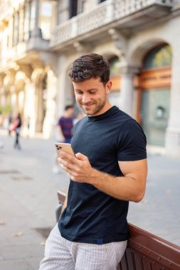 Şehir caddesinde akıllı telefon kullanan neşeli bir adam.