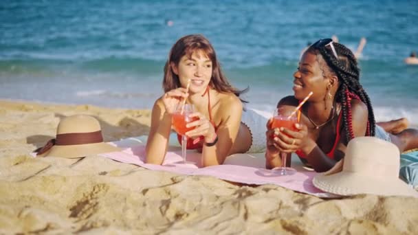 Zwei Mädchen liegen mit Fruchtcocktails am Strand — Stockvideo