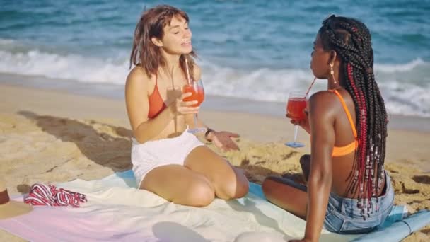 Due ragazze gioiose sedute sulla spiaggia di sabbia con cocktail — Video Stock