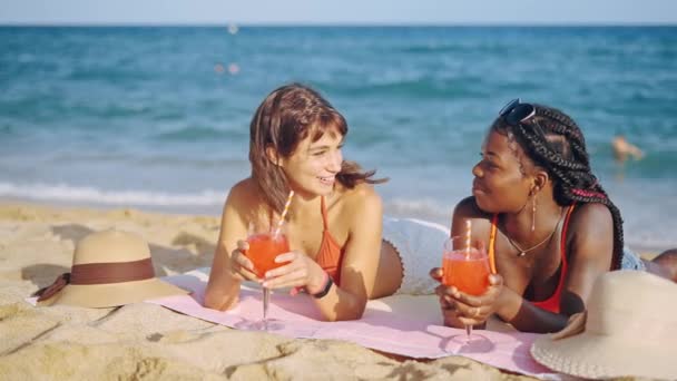 Две молодые многорасовые девушки лежат на песчаном пляже — стоковое видео