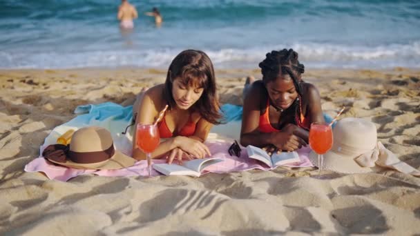 Zwei Studentinnen liegen mit offenen Büchern am Sandstrand — Stockvideo
