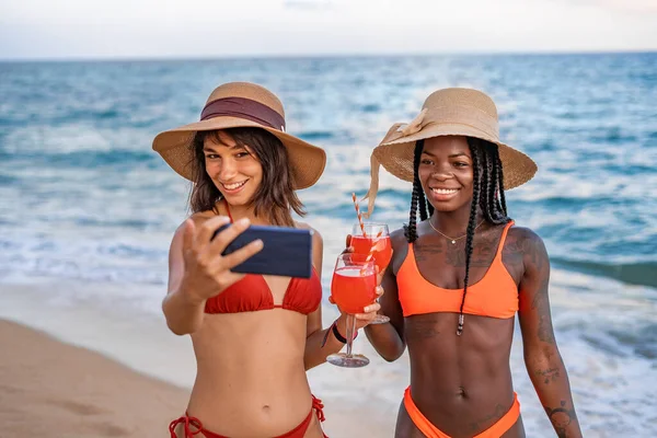 Contenidos novias con bebidas tomando selfie en la orilla del mar — Foto de Stock