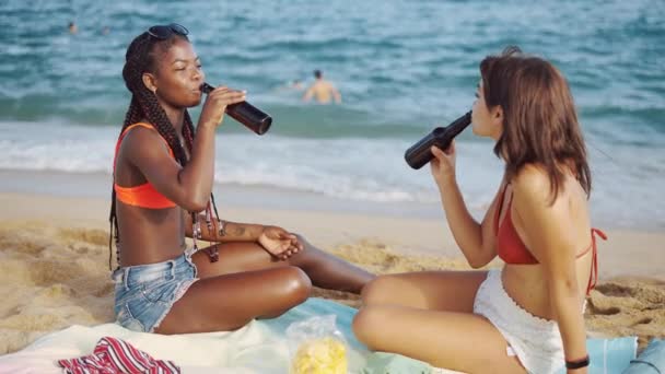 Bästa vänner som sitter på stranden och dricker ur flaskor — Stockvideo
